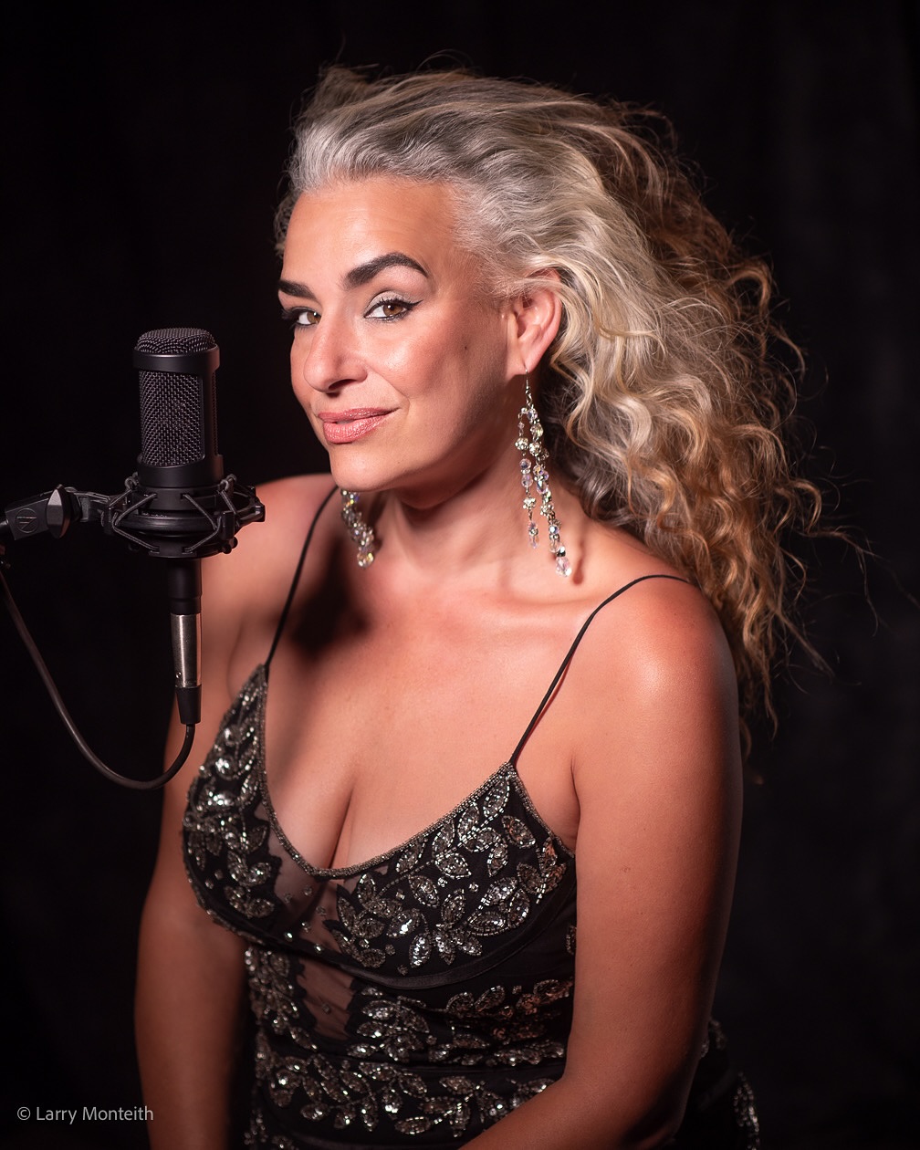 woman in a sparkly black dress poses with a microphone