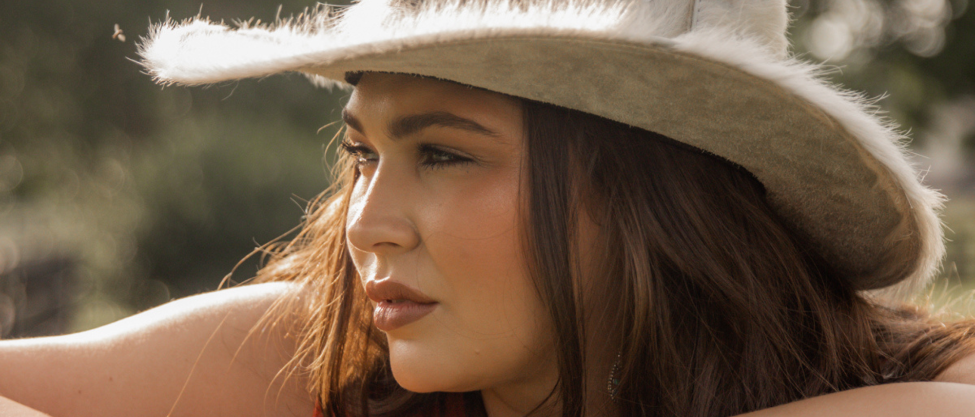 Kendall Lanford, country artist, stares off into the distance wearing a fuzzy cowboy hat