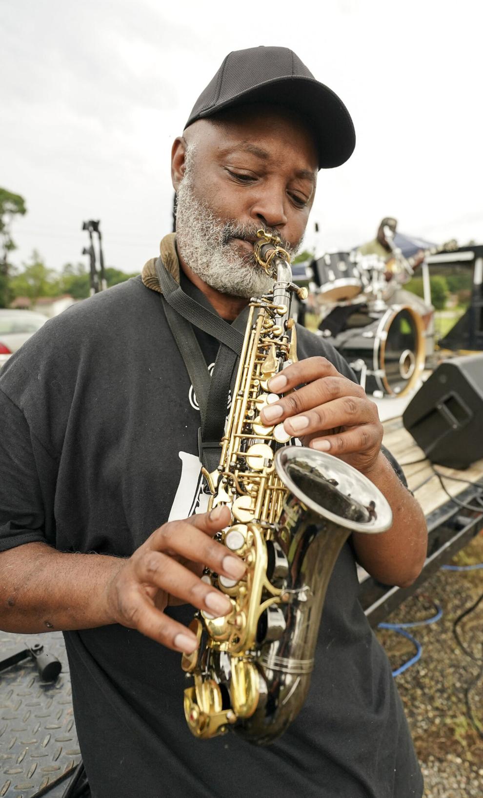 Man plays alto sax standing near a trailer.